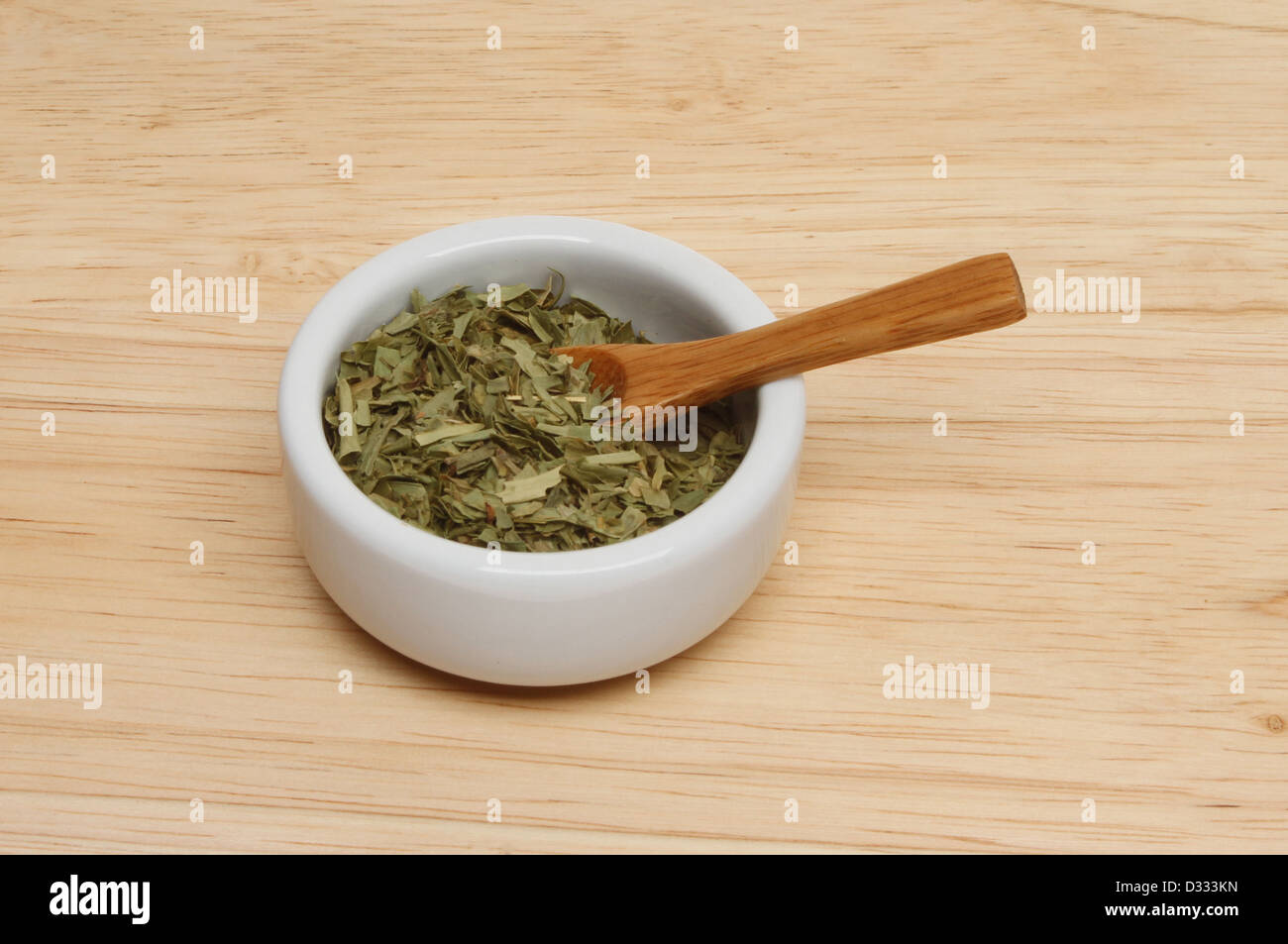 Essiccato di dragoncello foglie di erbe in un ramekin con un cucchiaio di legno su una tavola di legno Foto Stock