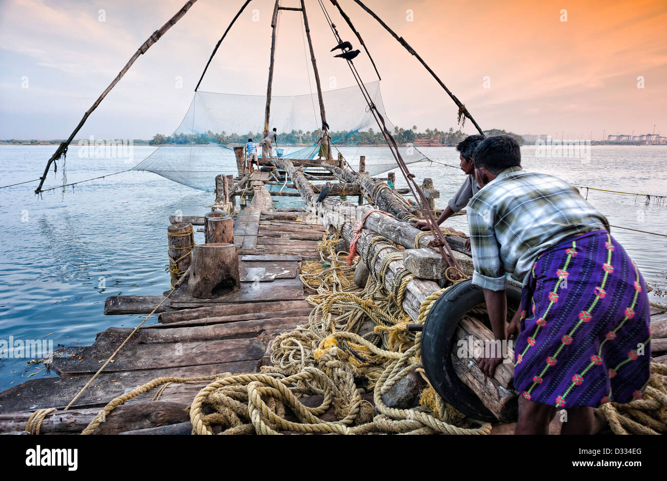 I pescatori operano un cinese vecchia rete da pesca nel porto di Fort Kochi, Kerala, India su un tardo pomeriggio in inverno. Foto Stock