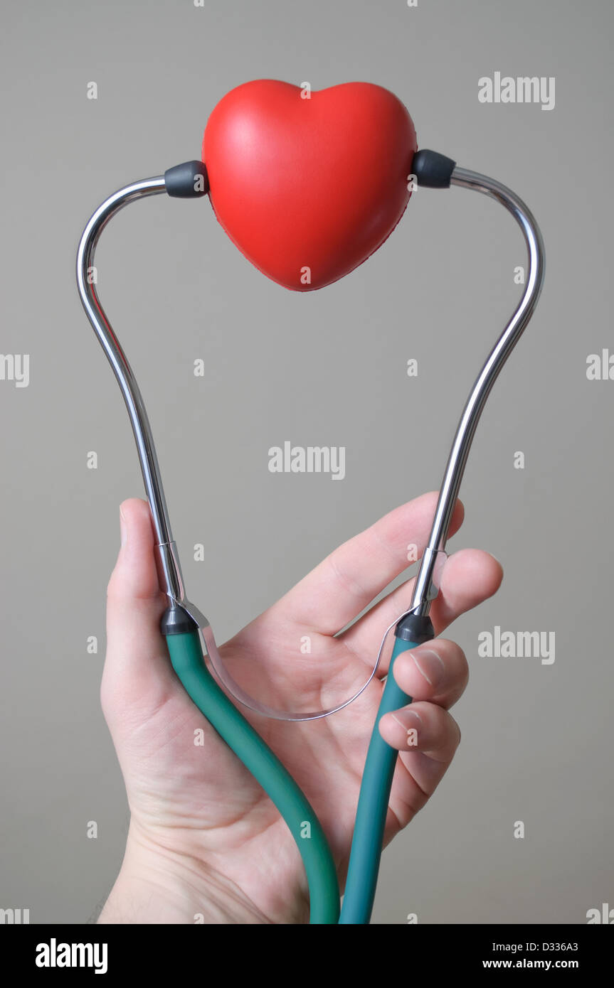 Mano d'uomo tenendo un cuore rosso forma e uno stetoscopio Foto Stock