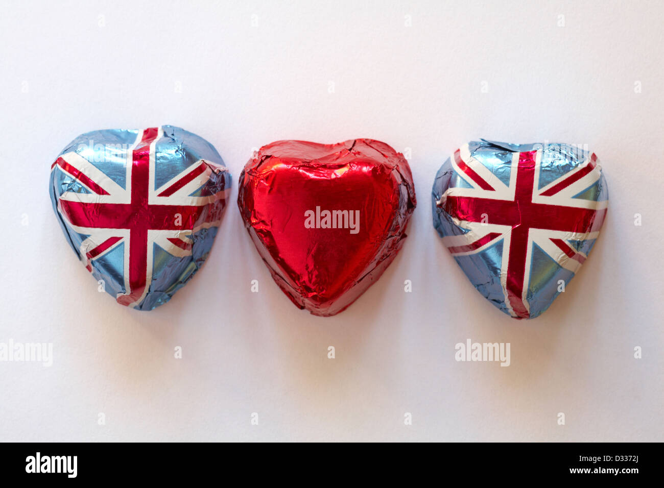 Tre a forma di cuore ad cioccolatini, due in Unione Jack involucro in foglio e uno in lamina di rosso isolato su sfondo bianco Foto Stock