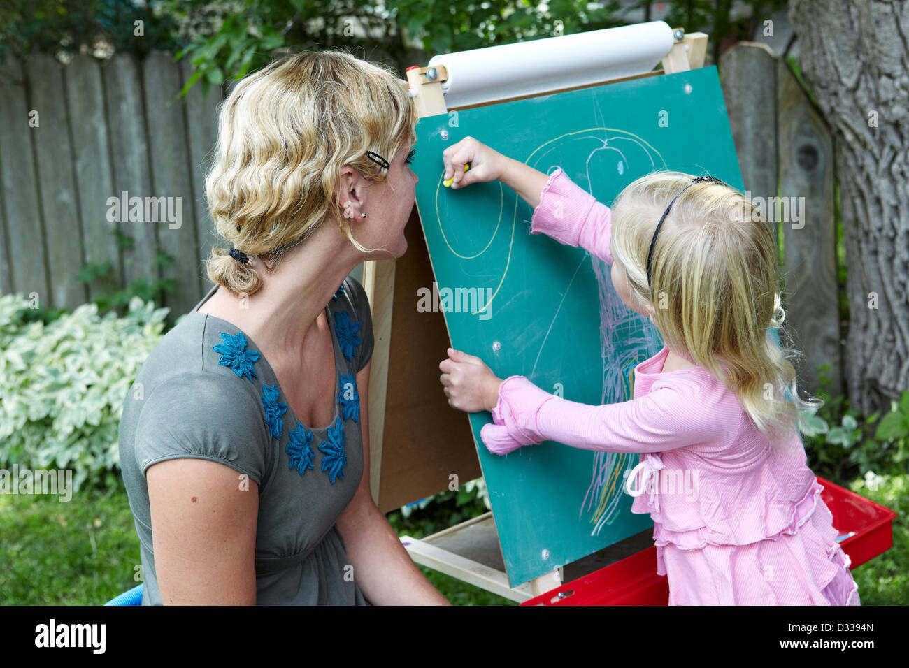 Madre guarda la figlia disegnare sulla lavagna Foto Stock