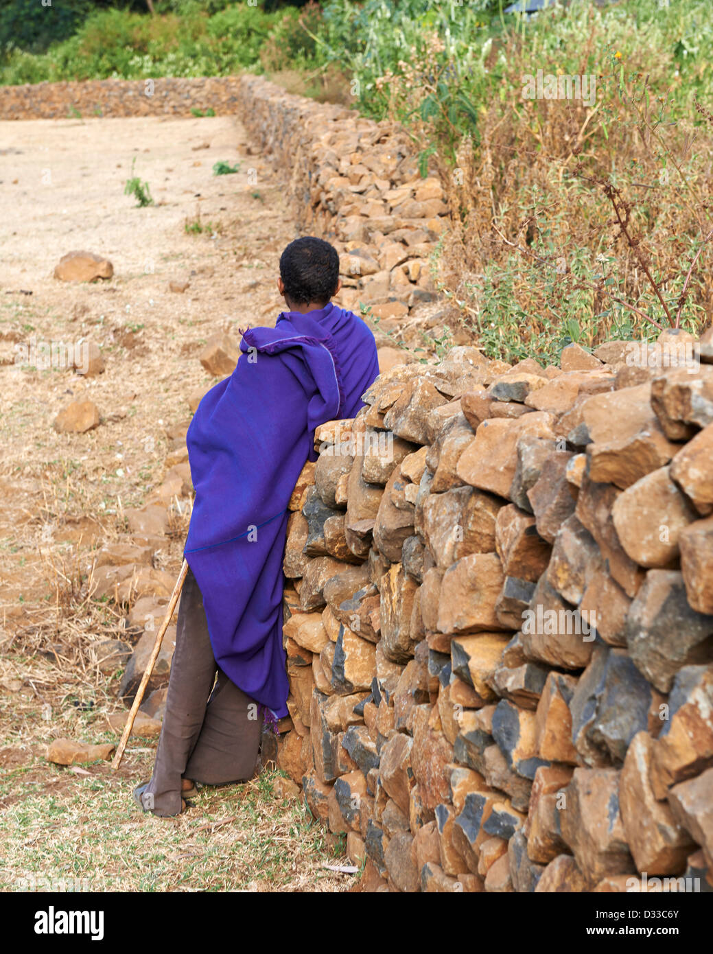 Un pellegrino che indossa un manto di porpora appoggiata contro il muro di pietra a Zara Foresta della Chiesa in Etiopia Foto Stock