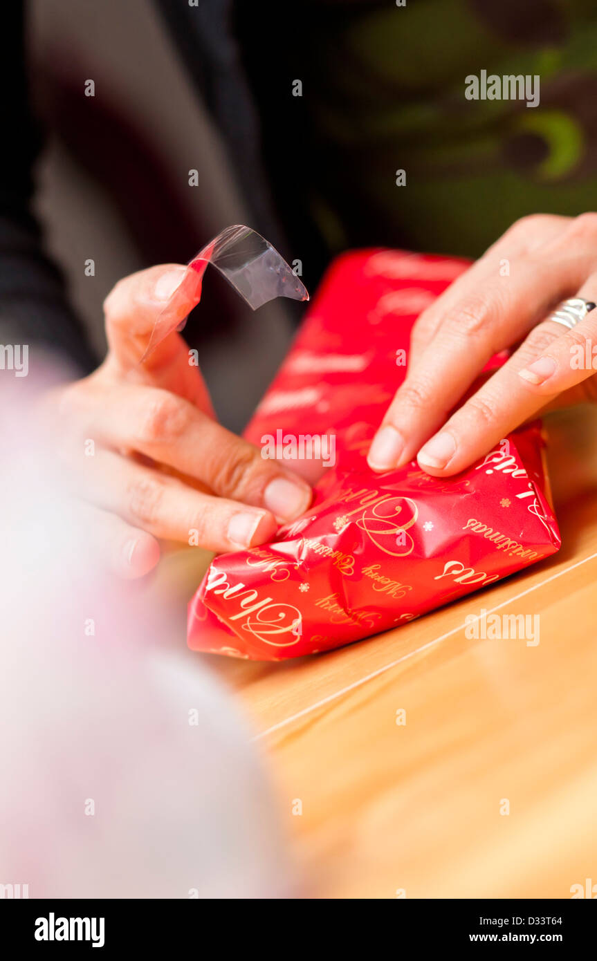 Preparatevi per il giorno di Natale. Avvolgere regali di Natale, dettagli delle mani con nastro adesivo e carta da imballaggio intorno a un regalo. Foto Stock