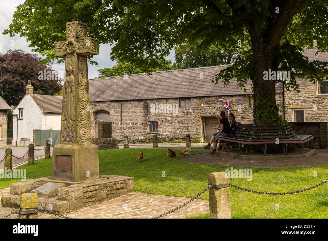 Due persone sedute su posti a sedere in legno sotto agli alberi con pietra memoriale di guerra in primo piano nel villaggio di Castleton Derbyshire Foto Stock