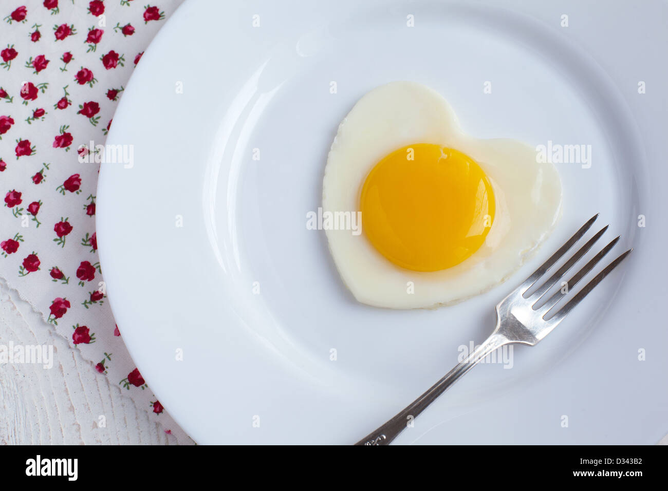 Uovo fritto a forma di cuore in una piastra bianca con una forcella Foto Stock