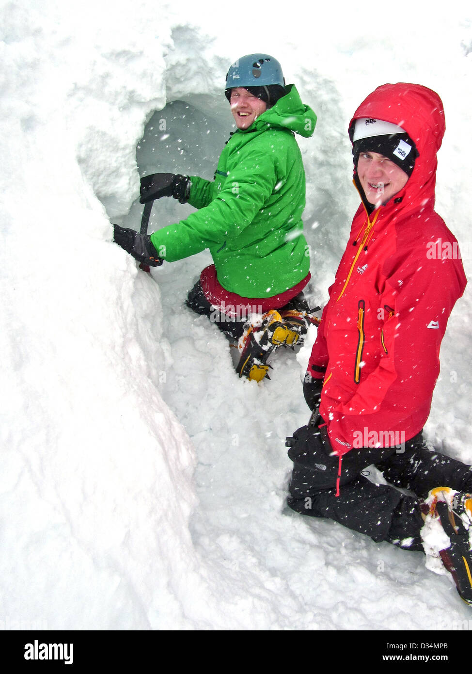 Due giovani uomini scavare un foro di neve nelle highlands scozzesi Foto Stock