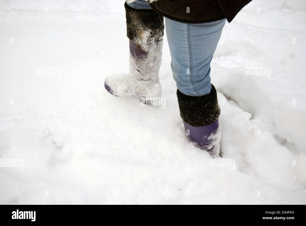 La donna a piedi attraverso la neve in stivali da pioggia Foto Stock