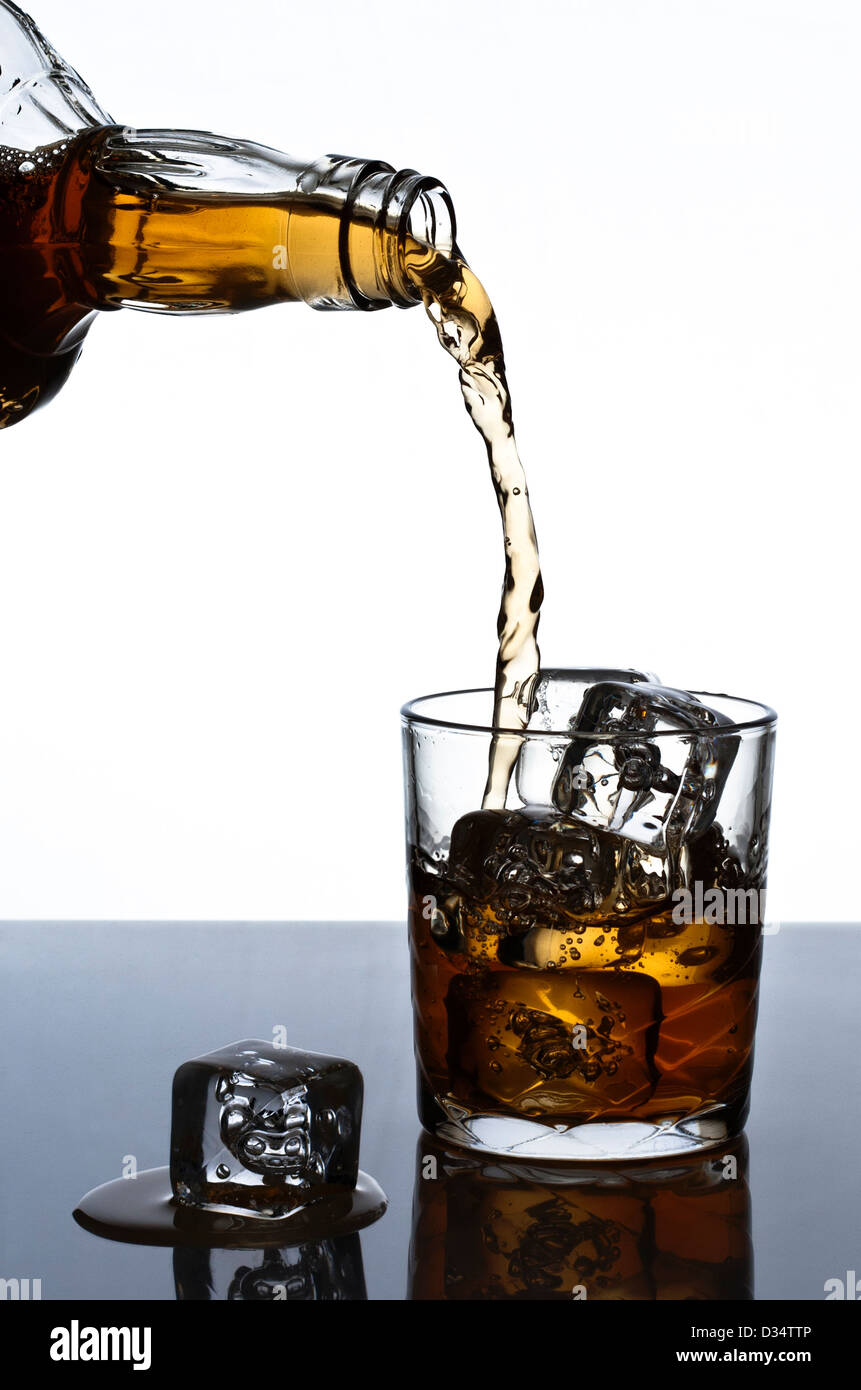 Una bottiglia di whiskey essendo versare in un bicchiere di ghiaccio. Foto Stock