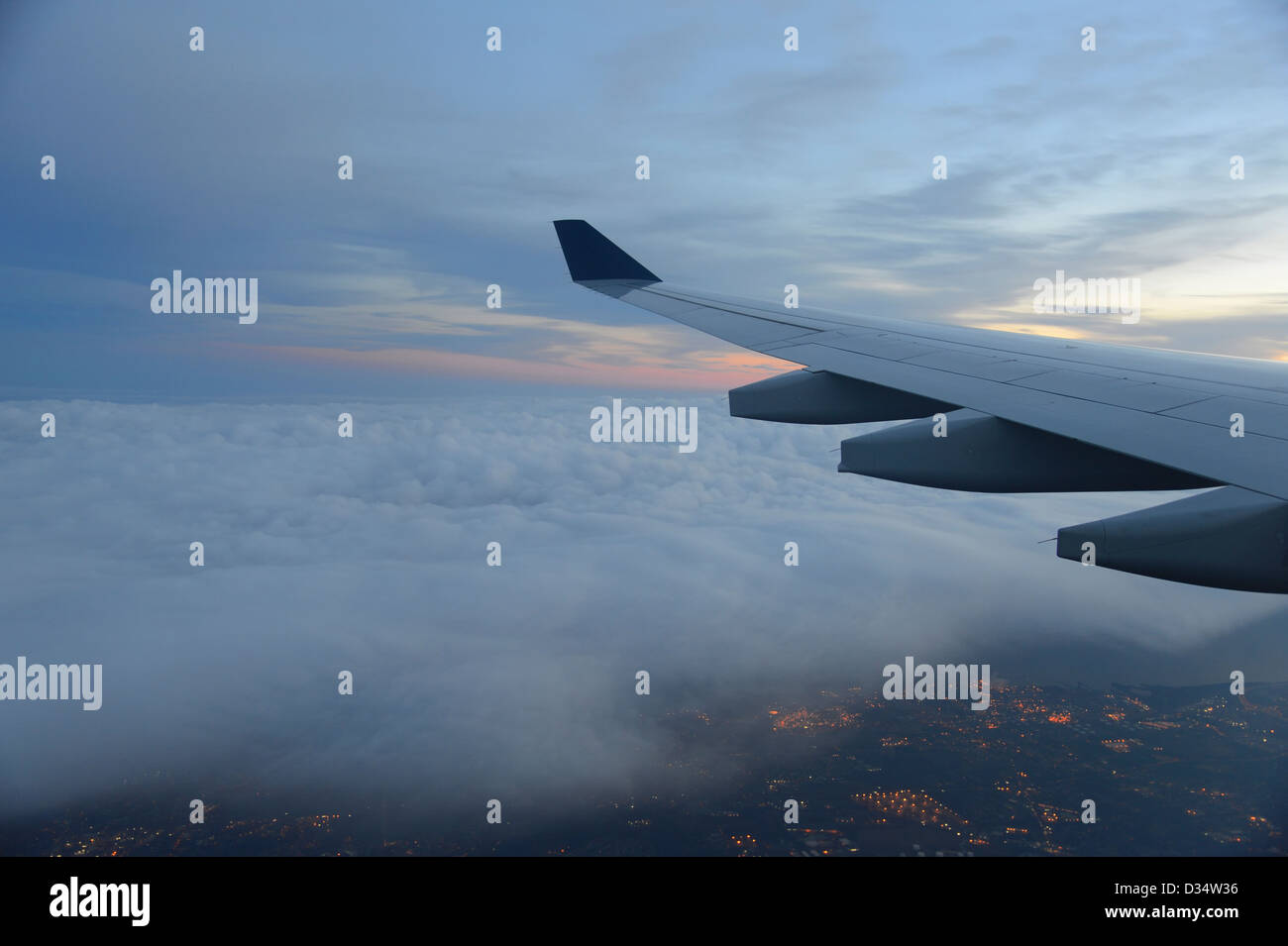Ala di aeroplano e tramonto nuvole, luci della città al di sotto di Foto Stock