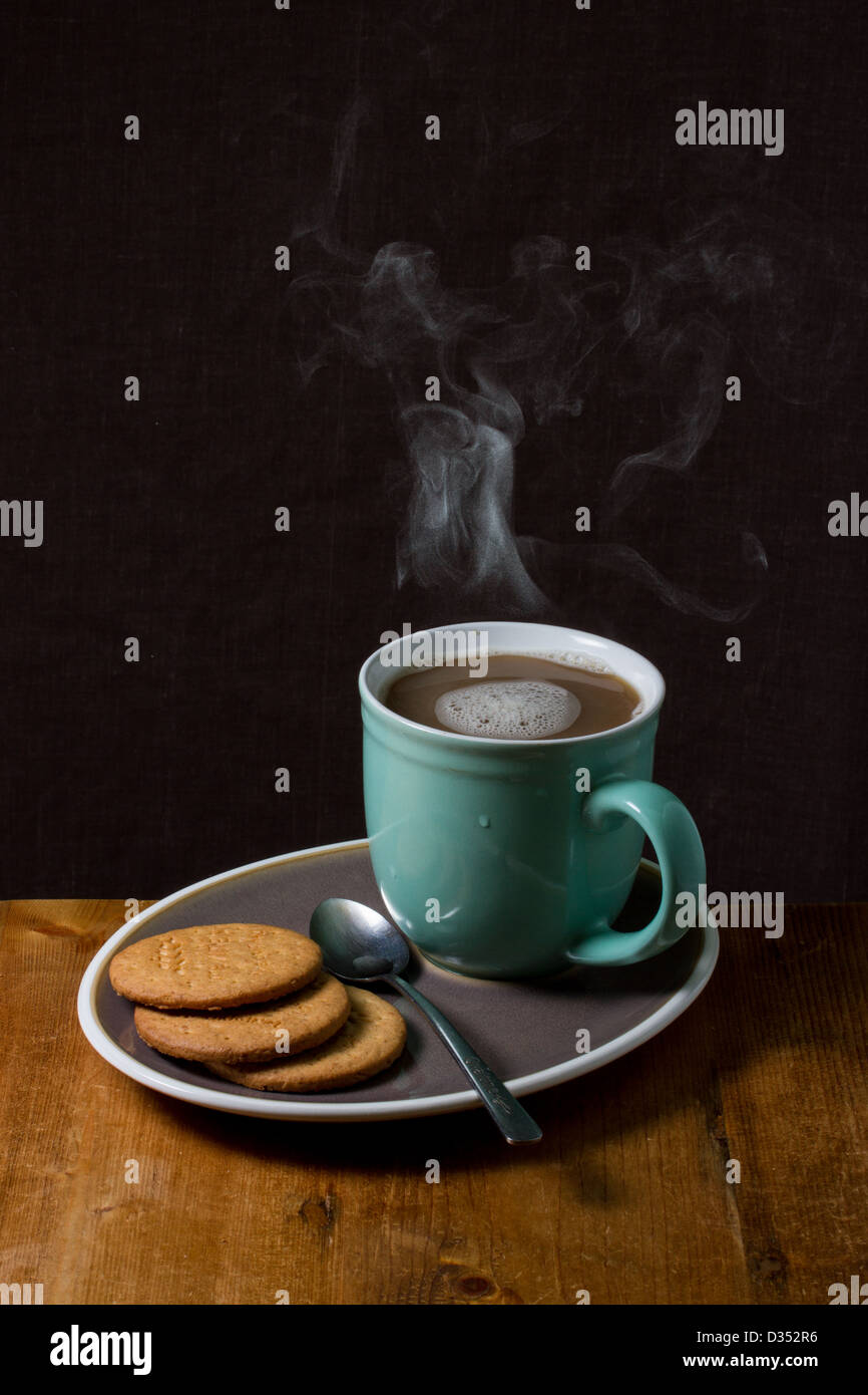 Una fumante tazza di una bevanda calda su un piattino con biscotti Foto Stock