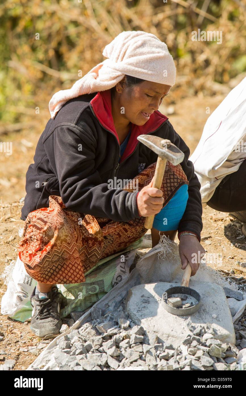 Una donna Nepalese la frantumazione di pietra con un martello, foothills dell'Himalaya, Nepal. Foto Stock