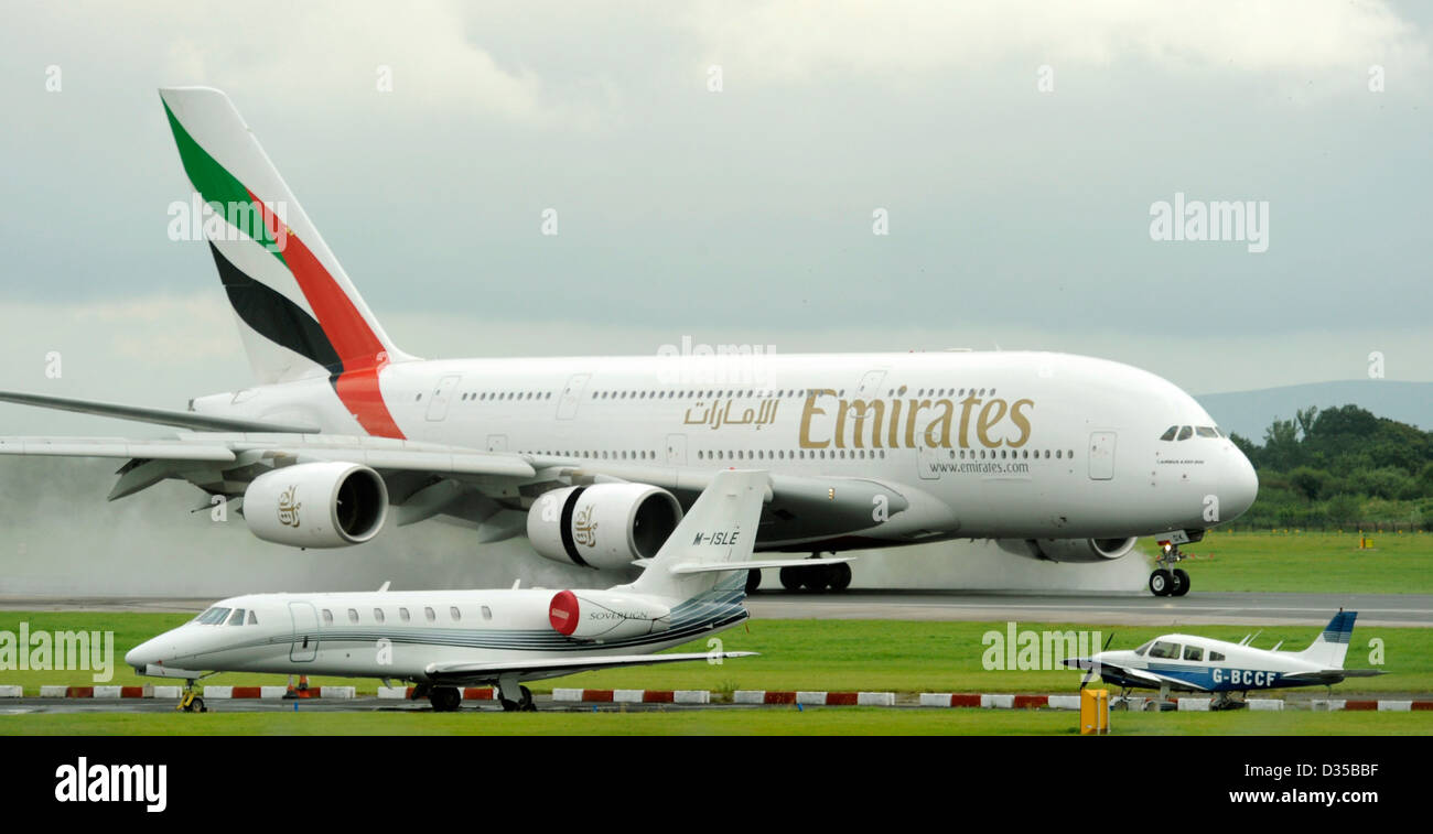 Emirates Airlines Airbus A380 861 E6 EDK atterra su una pista bagnata all'Aeroporto di Manchester che mostra la scala con jet privato piccolo aereo Foto Stock