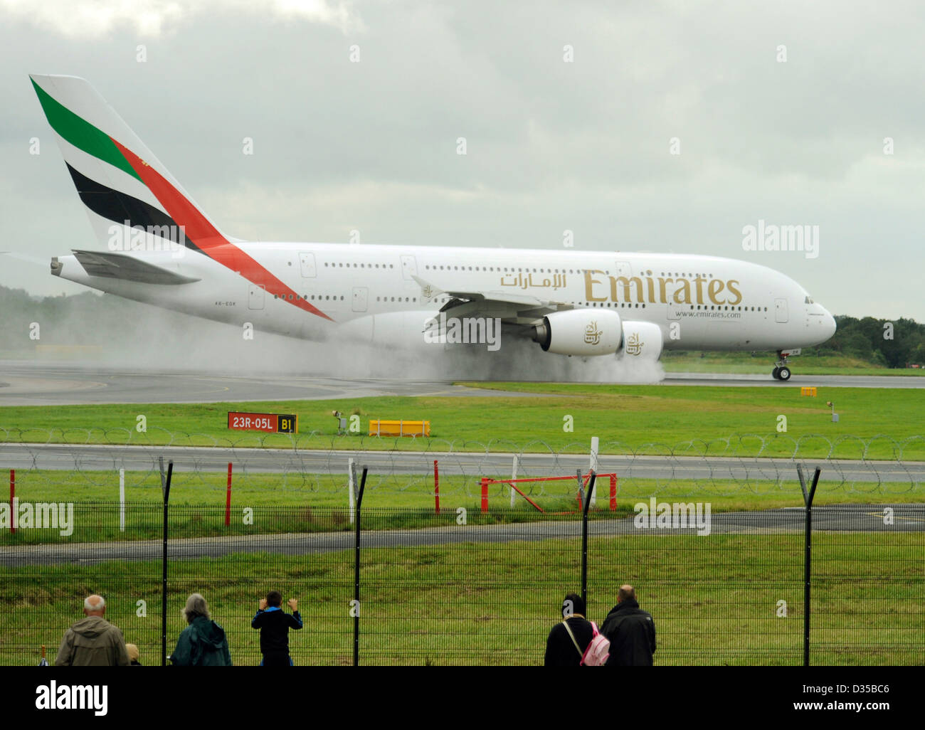 Persone e appassionati di aerei guarda la Emirates Airlines Airbus A380 861 E6 EDK atterrare su una pista bagnata all'Aeroporto di Manchester Foto Stock