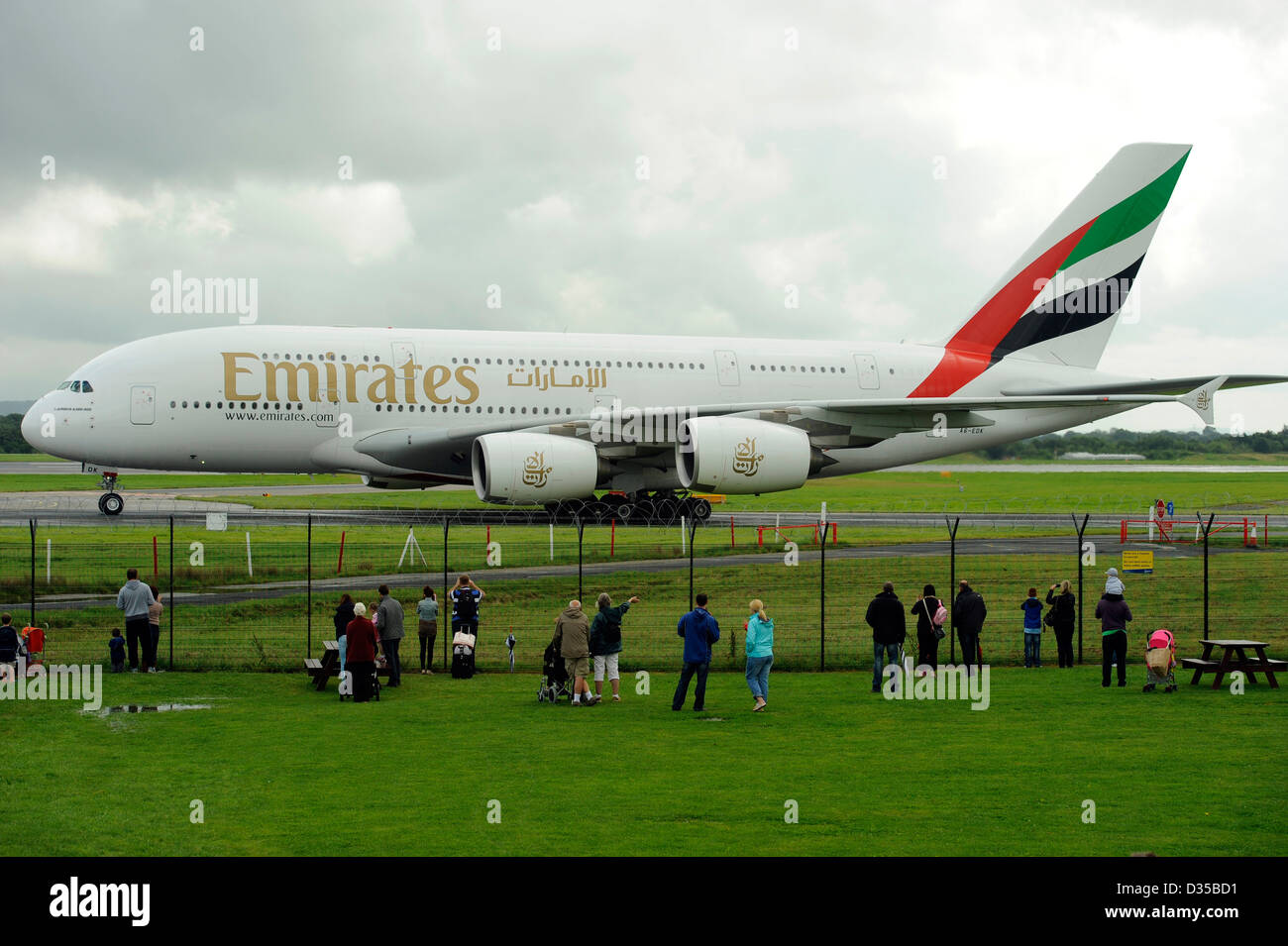 Persone e appassionati di aerei guarda la Emirates Airlines Airbus A380 861 E6 EDK atterrare su una pista bagnata all'Aeroporto di Manchester Foto Stock