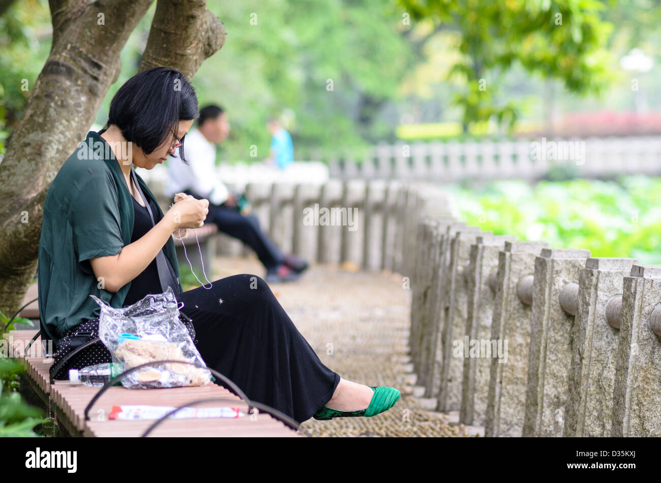 Donna cinese di effettuare il suo hobby - cucire - in un parco pubblico Foto Stock