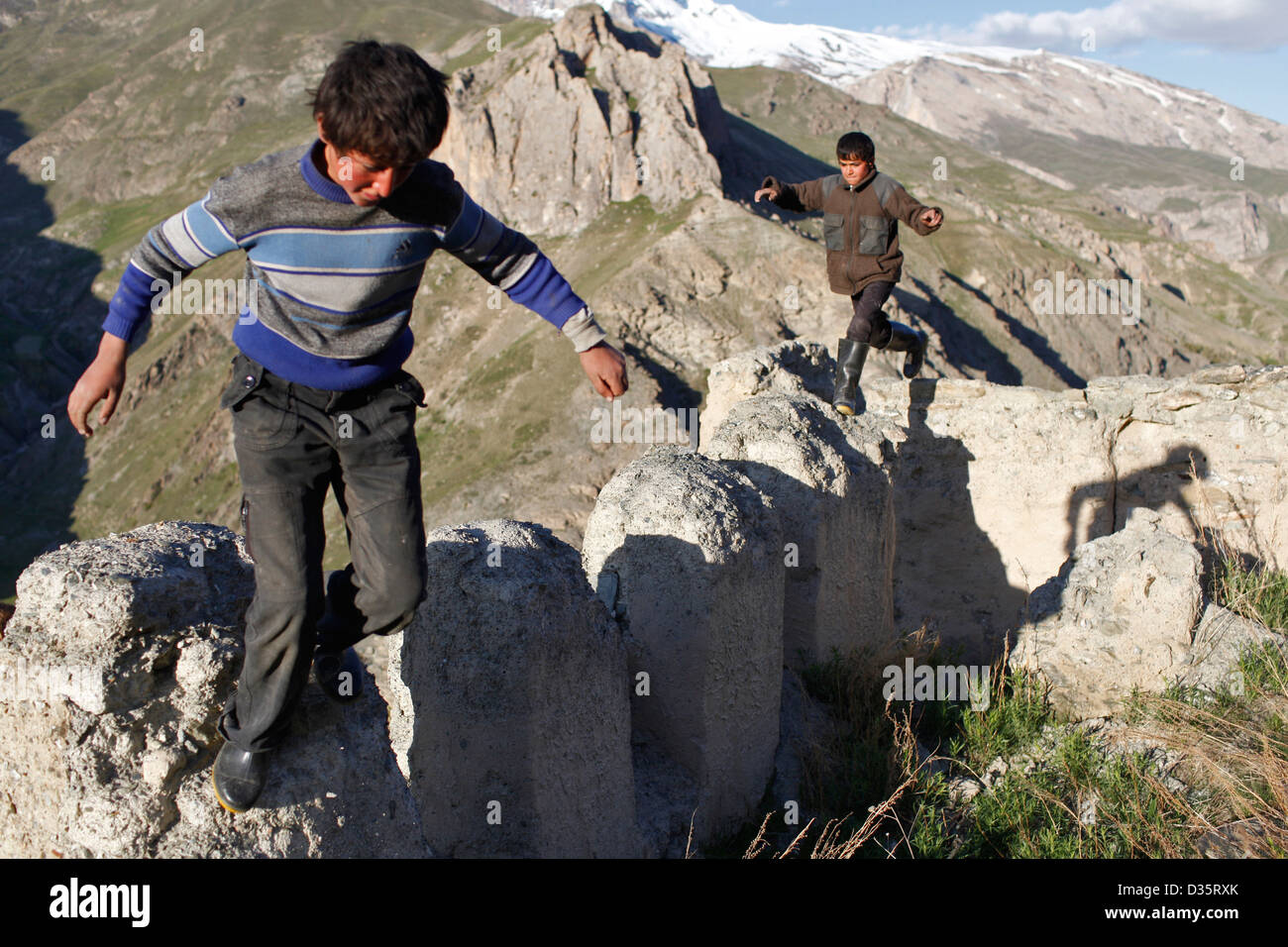 Yagnobi boys hop tra parti di una vecchia casa in rovine del villaggio Chukkat, Tagikistan Foto Stock