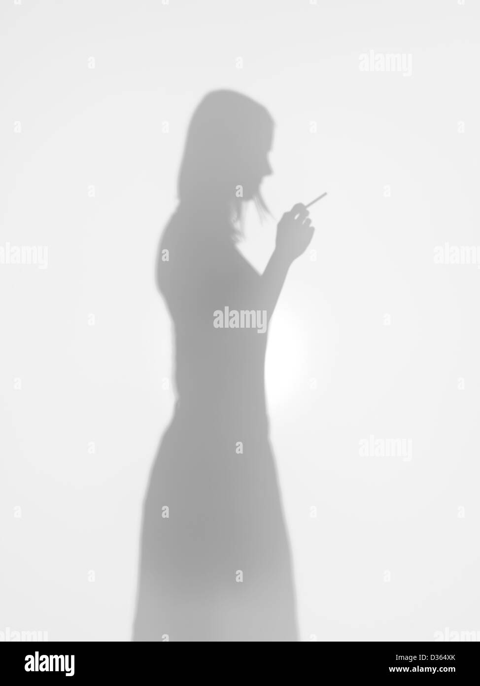 Silhouette di donna in piedi con una sigaretta in mano dietro una superficie diffusa, vista laterale Foto Stock