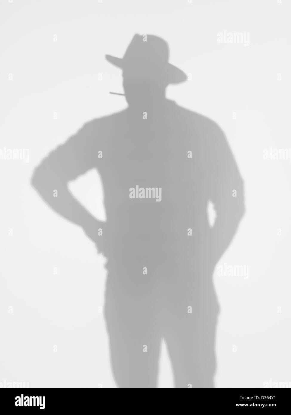 Silhouette uomo in piedi e in posa con un cappello da cowboy e fumare una sigaretta dietro una superficie diffusa Foto Stock