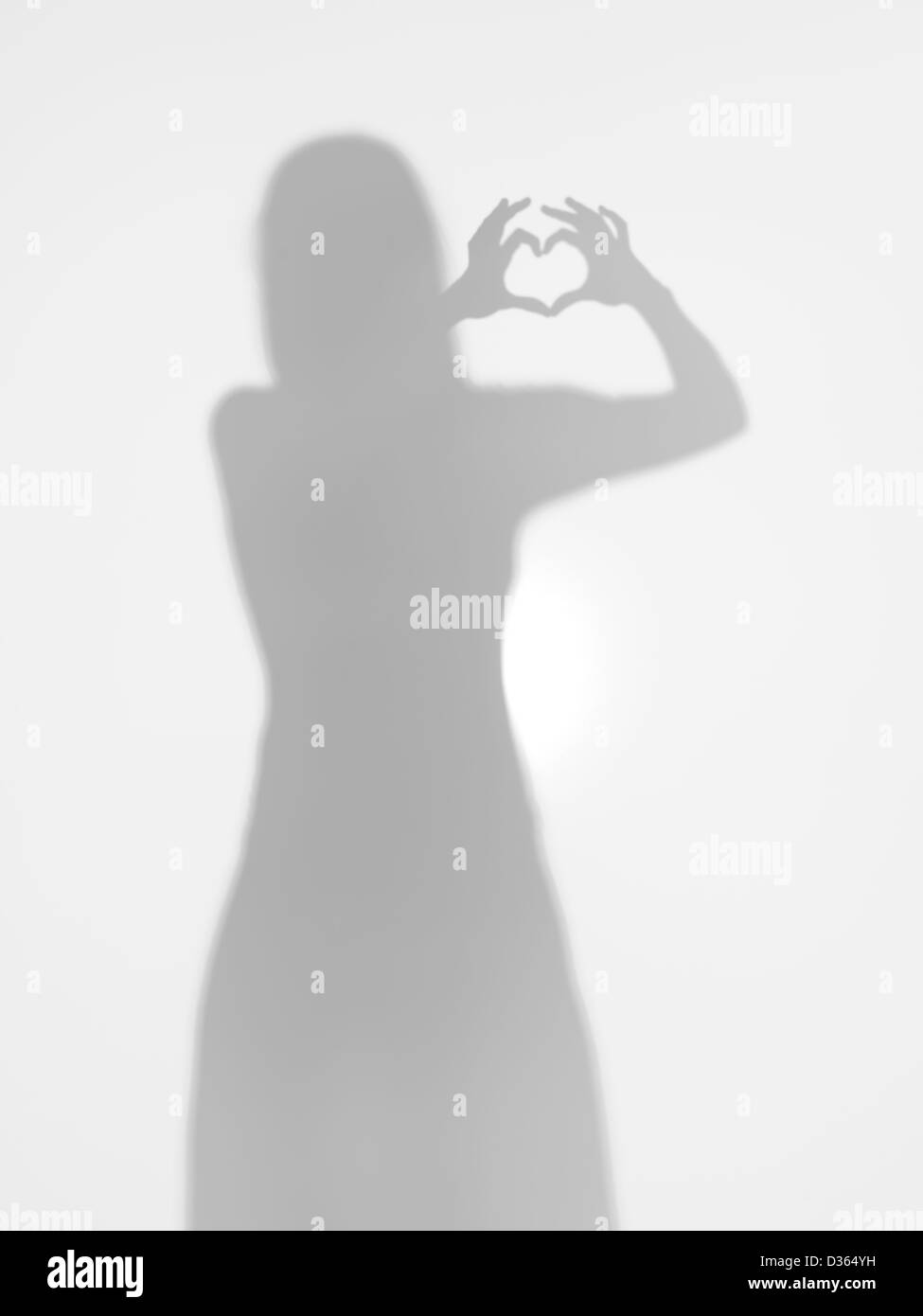 Corpo femmina creatind silhouette a forma di cuore con le sue mani, dietro una superficie diffusa Foto Stock