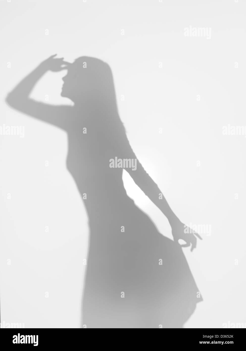 Corpo femmina silhouette guardando lontano e tenendo premuto il suo vestito elegantemente con una mano, dietro una superficie diffusa Foto Stock