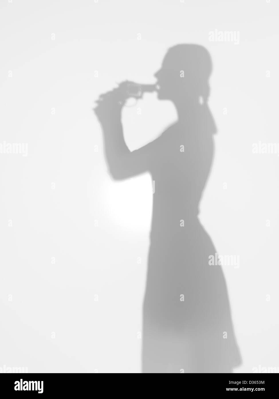 Vista laterale del corpo femmina silhouette in possesso di una pistola contro la sua bocca di suicidarsi, dietro una superficie diffusa Foto Stock