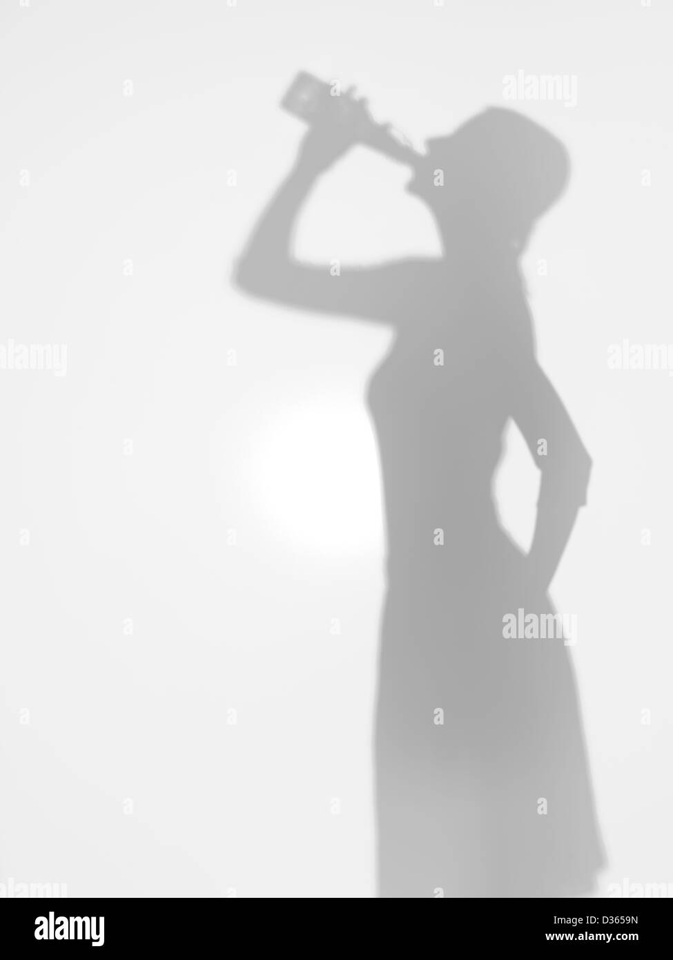Giovane ragazza a bere birra da una bottiglia di vetro, silhouette, dietro una superficie diffusa Foto Stock