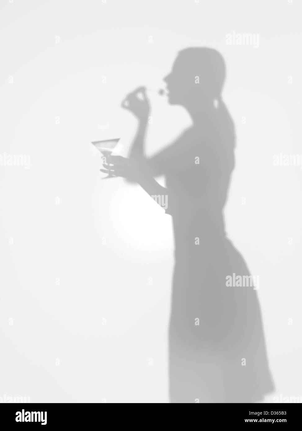 Vista laterale della silhouette femmina tenendo un coppetta Martini in mano di mangiare un'oliva, dietro una superficie difuse Foto Stock