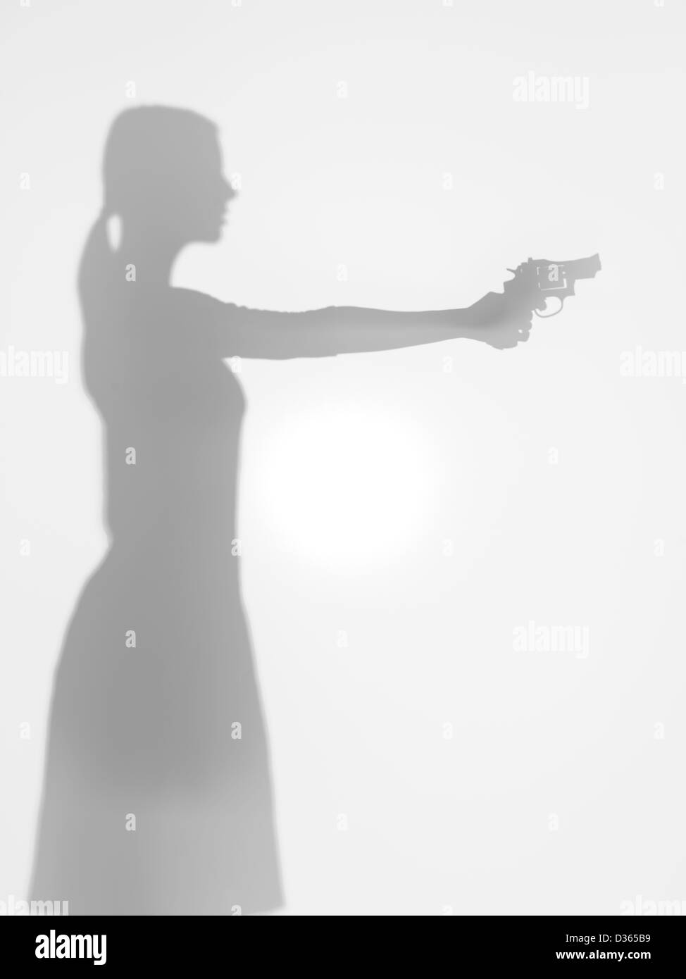 Vista laterale della silhouette di donna in possesso di una pistola mirando davanti a lei, dietro una superficie diffusa Foto Stock