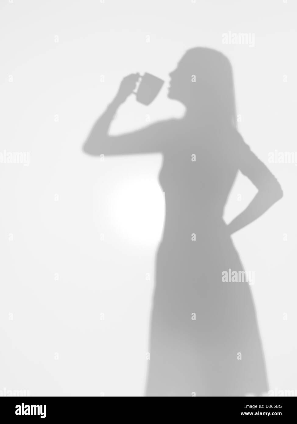 Vista laterale della silhouette di donna di bere il caffè da una tazza dietro una superficie diffusa Foto Stock