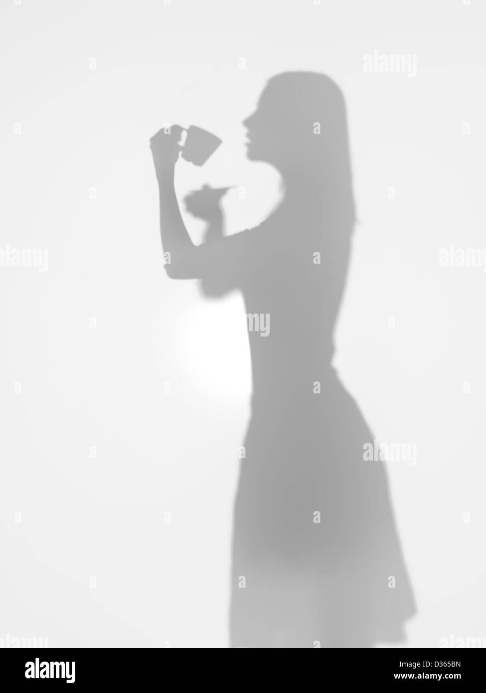 Vista laterale della silhouette di donna di bere una tazza di caffè dietro una superficie diffusa Foto Stock