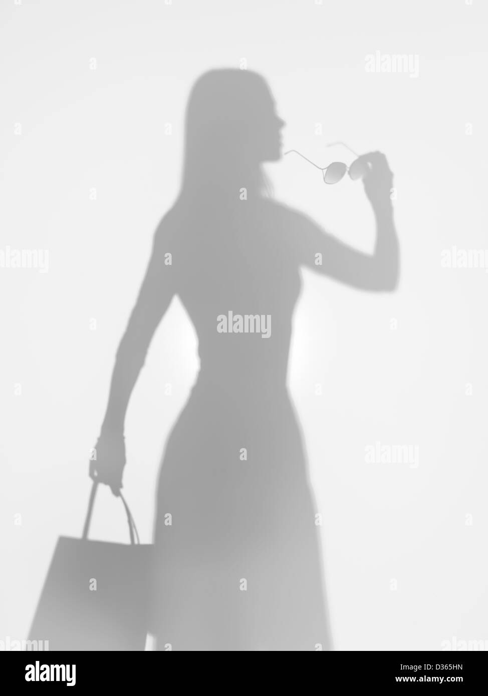Vista laterale di eleganti donna slim tenendo un sacco e un paio di occhiali da sole in mano dietro una superficie diffusa, silhouette Foto Stock