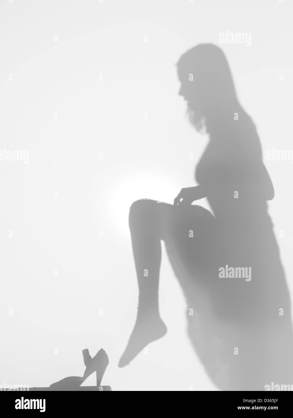 Vista laterale della donna che sta provando una scarpa tenendo la sua gamba in alto dietro una superficie diffusa Foto Stock