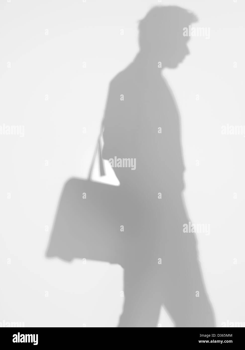 Vista laterale dell'uomo di affari che trasportano un sacco a spalla e a piedi, dietro una superficie diffusa Foto Stock