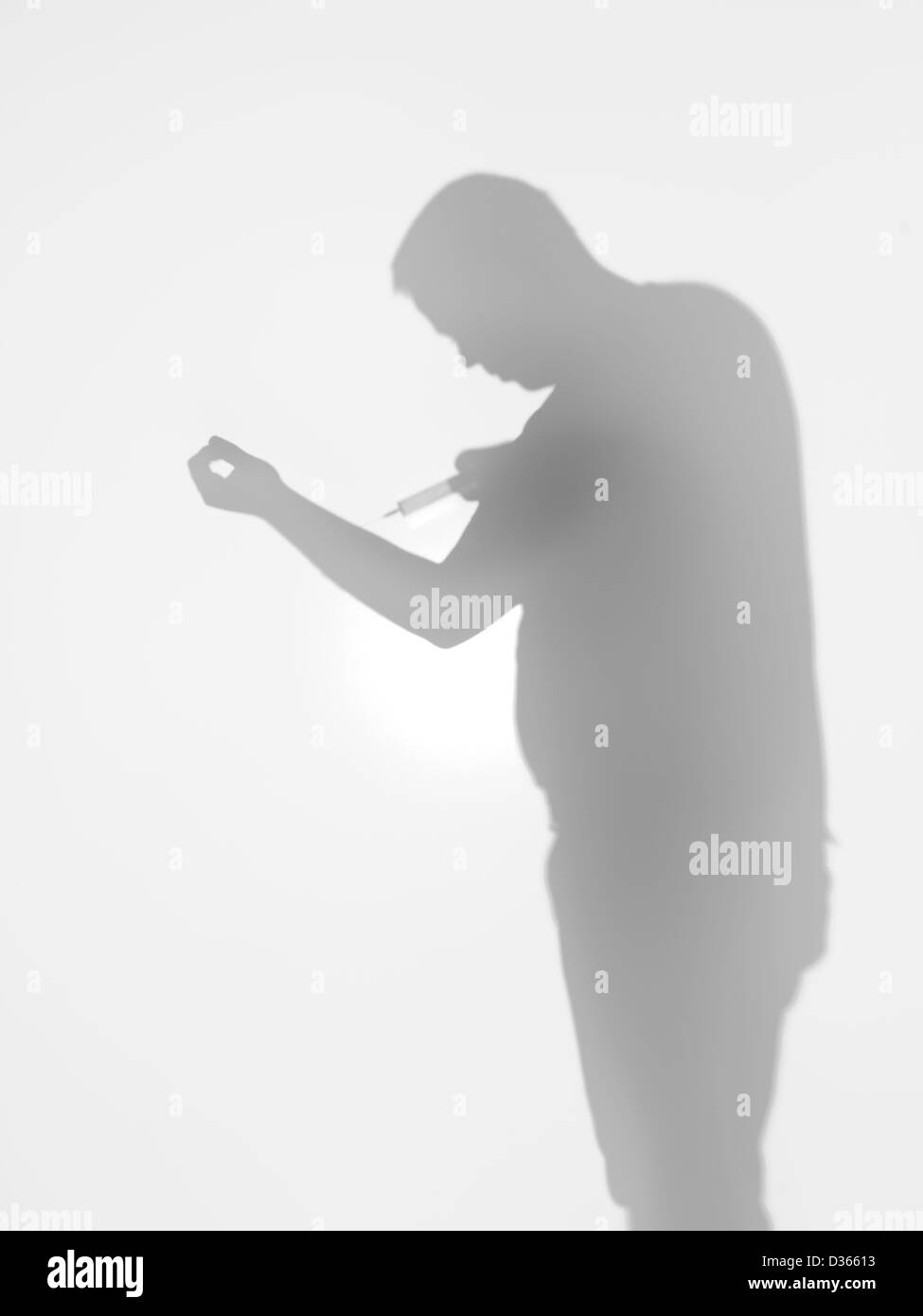 Vista laterale di uomo con una siringa verso il suo braccio dietro una superficie diffusa Foto Stock