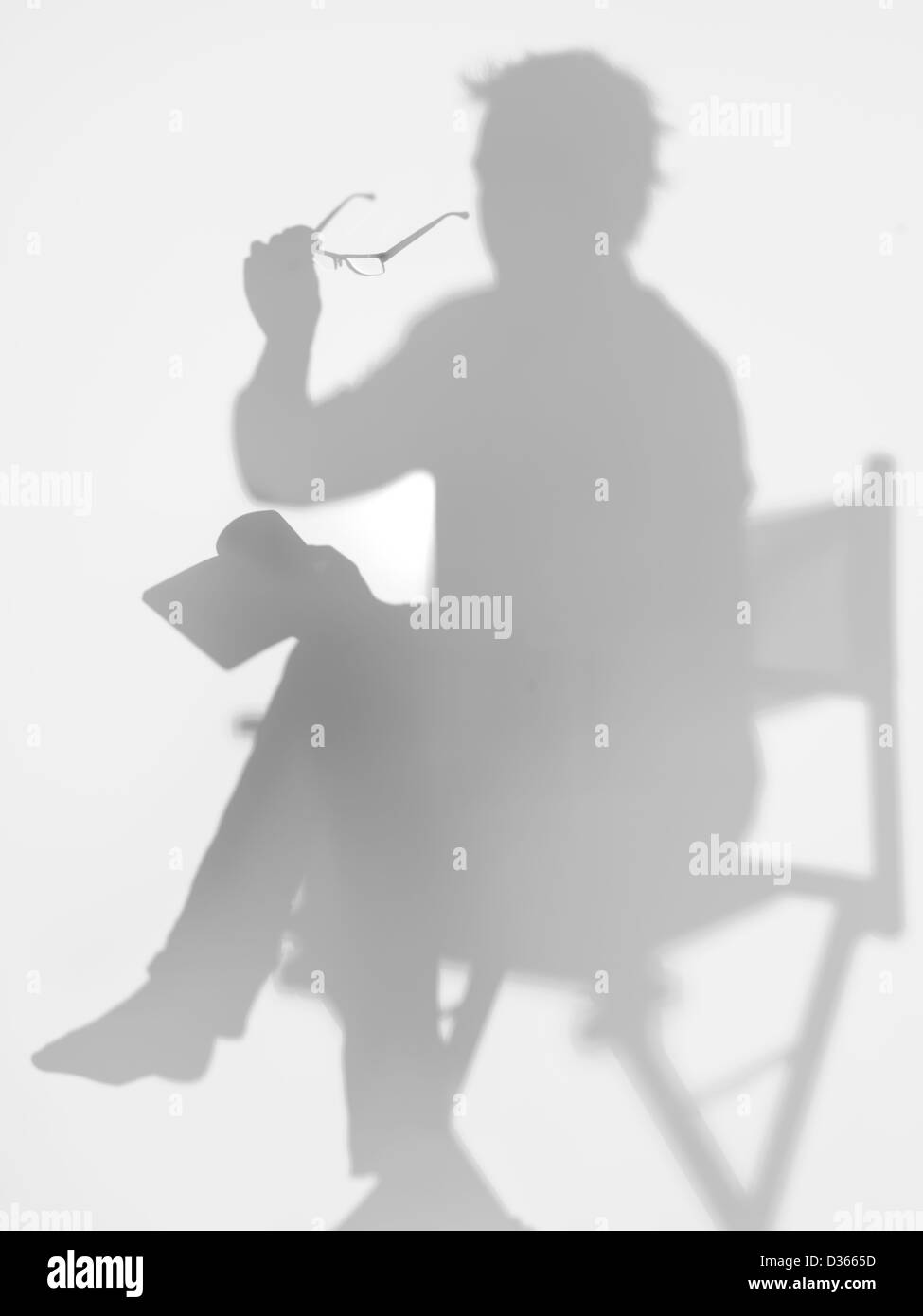 Uomo seduto sul direttore di sedia la lettura di un libro con gli occhiali in mano, dietro una superficie diffusa Foto Stock