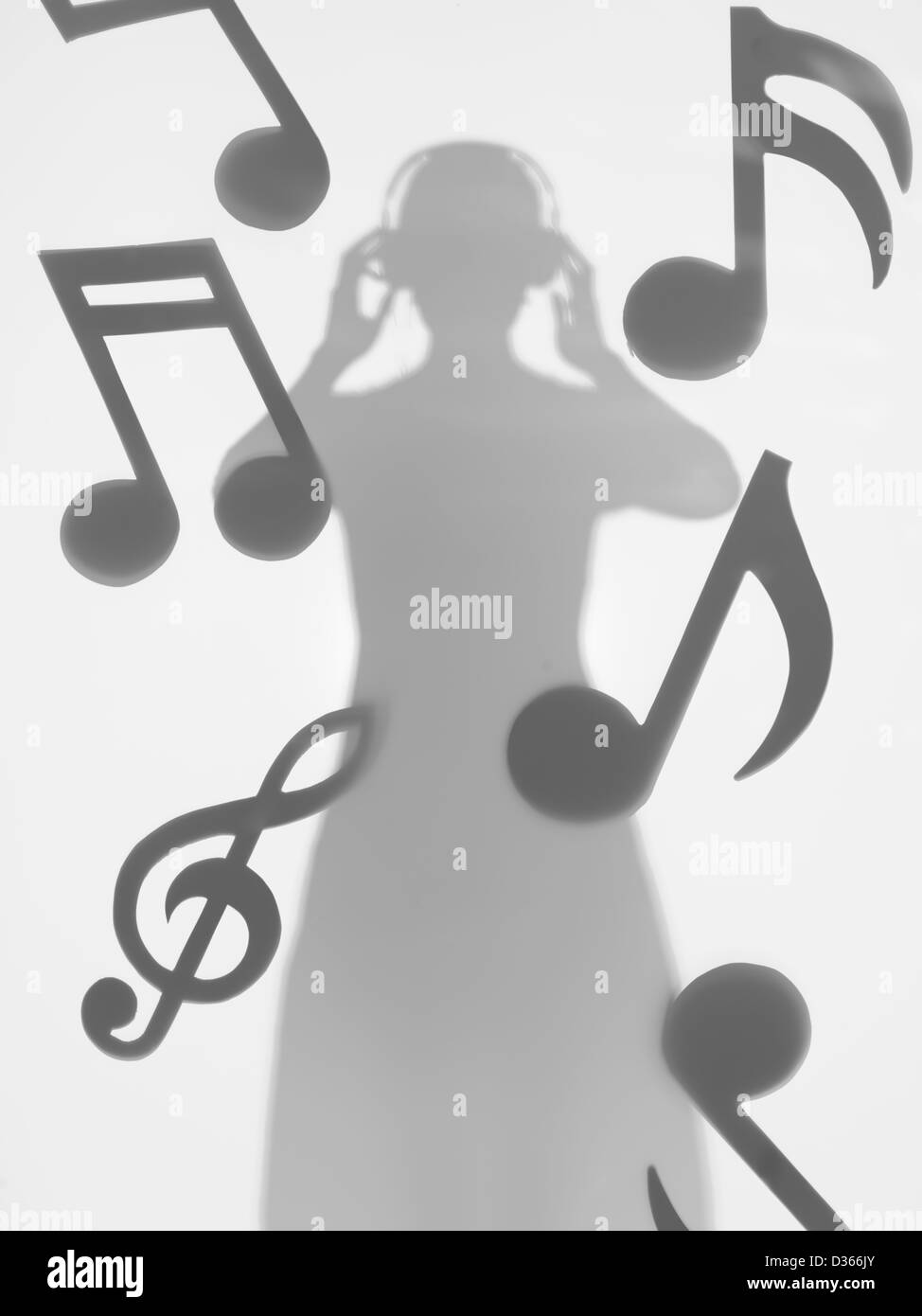 Donna in piedi e ascolto di musica con cuffie, tra le note musicali, dietro una superficie diffusa Foto Stock