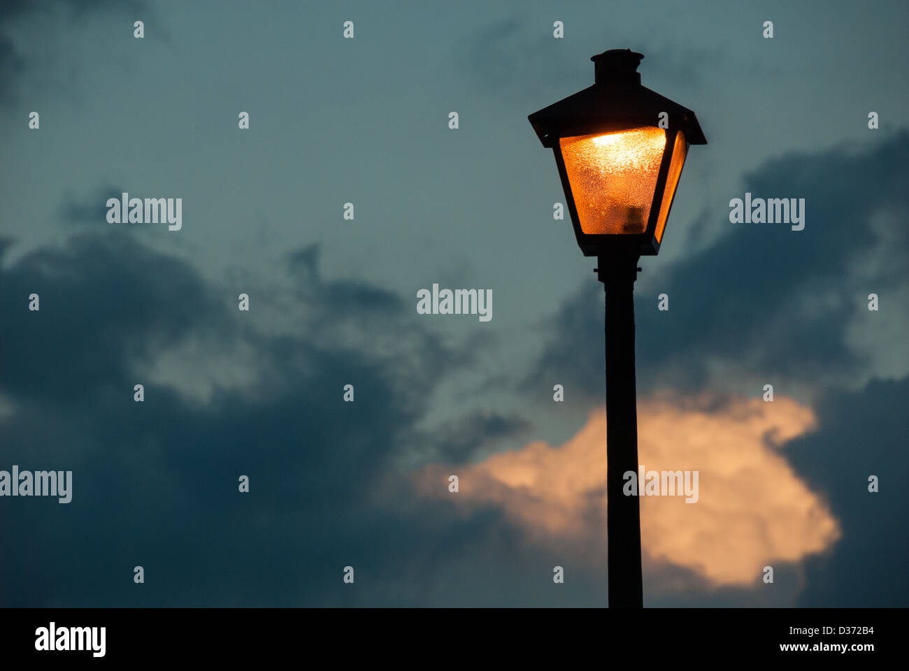 La luce calda proveniente da una lampada posta appare per illuminare una nuvola nell'ultima luce del crepuscolo. Foto Stock La luce calda proveniente da una lampada posta appare per illuminare una nuvola nell'ultima luce del crepuscolo. Foto Stock