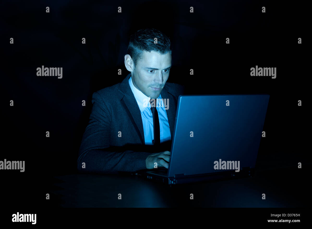 Un uomo sorridente lavorando su un computer portatile durante la notte o in una stanza buia Foto Stock