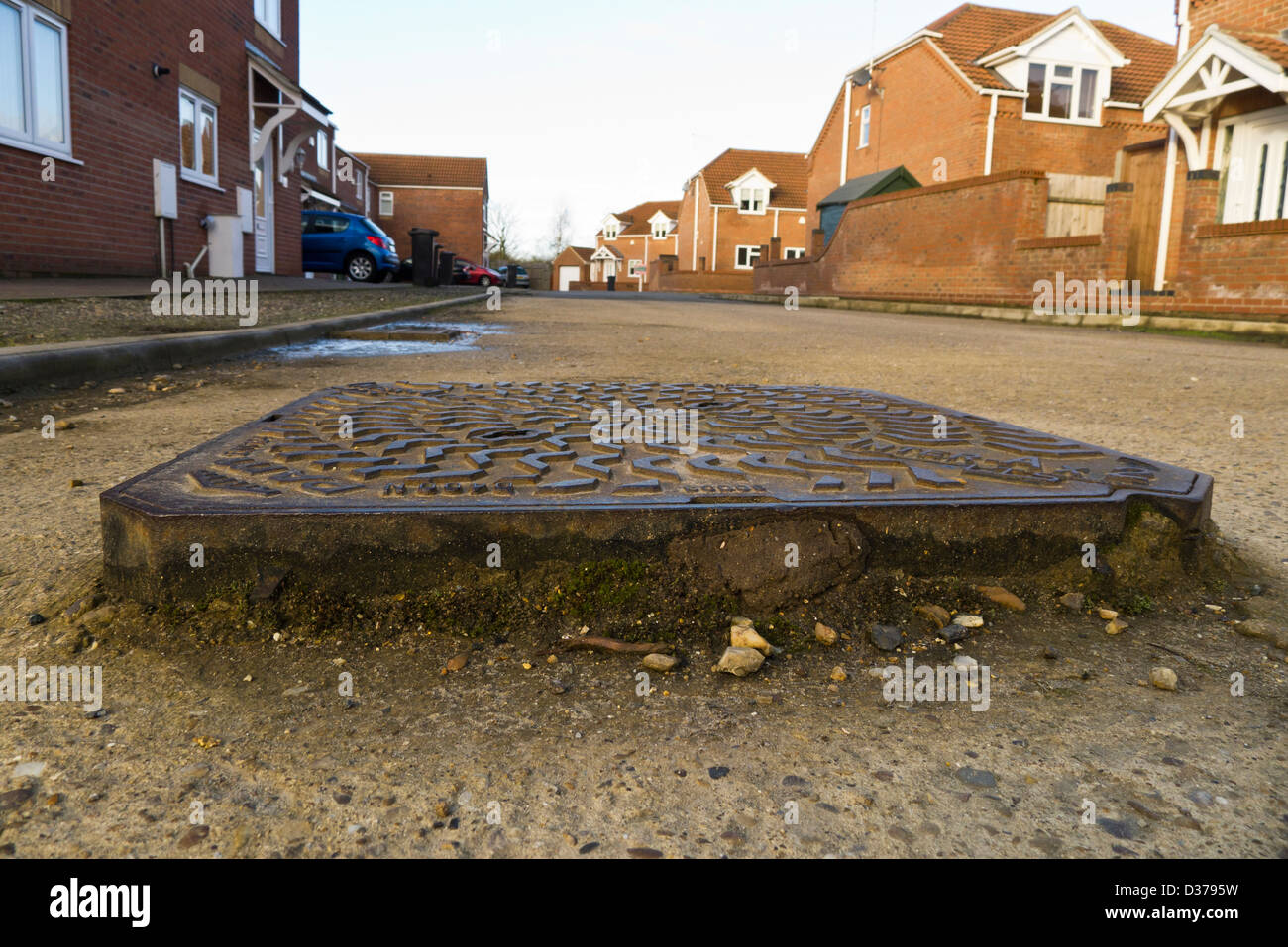 Un tombino sollevato il coperchio su una cattiva strada asfaltata in King's Lynn, Norfolk. Foto Stock