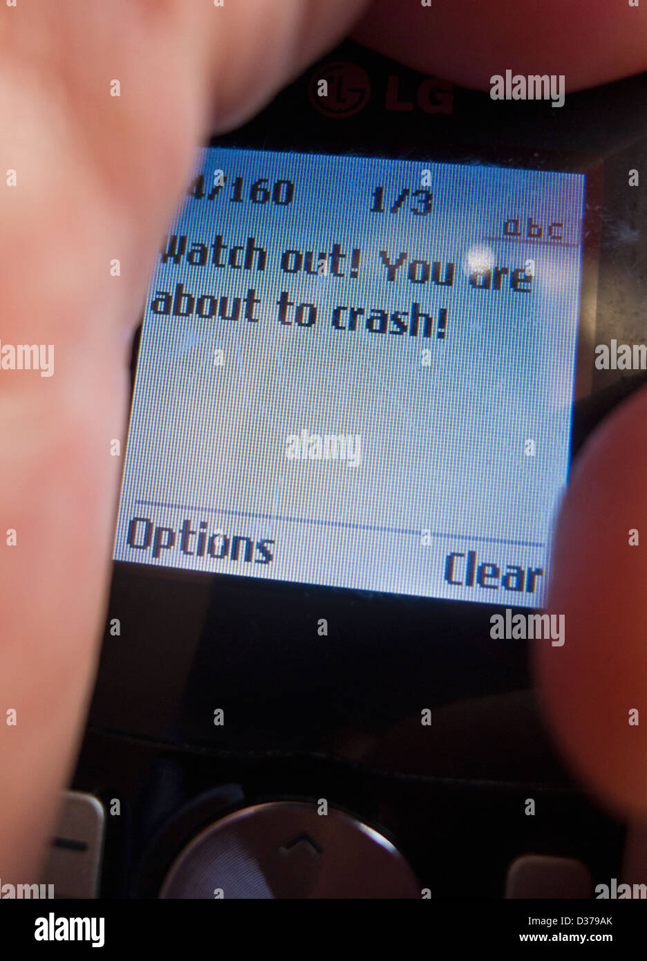 Telefono cellulare che mostra un messaggio di testo "watch out! Stai per andare in crash.' nella mano di un uomo alla guida. Foto Stock