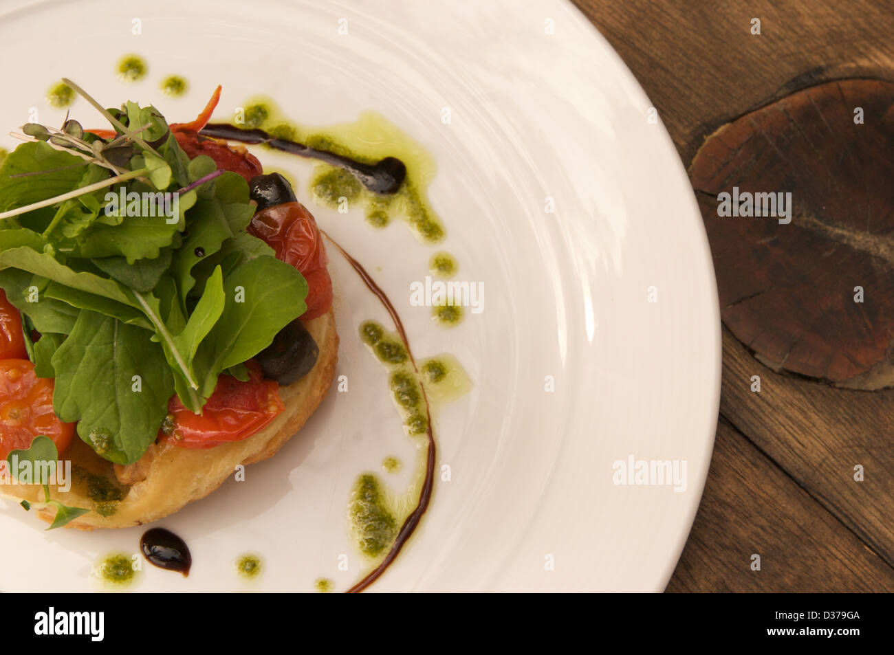 Pomodoro e olive Tarte tatin con insalata di rucola, sciroppo balsamico e pesto di rucola servita su una piastra bianca. Foto Stock