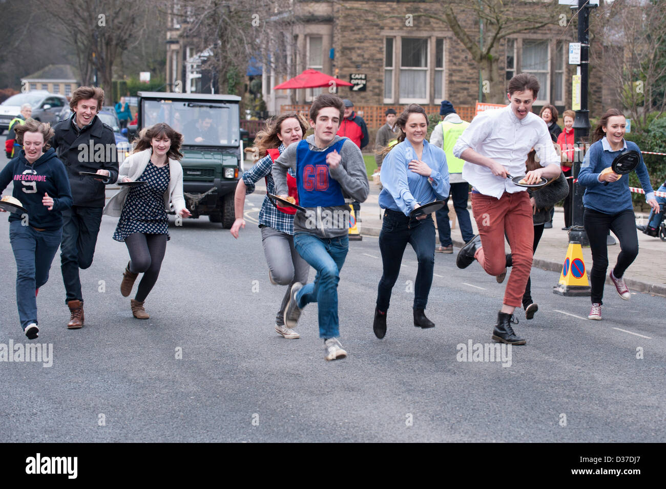 Concorrenti (maschile e femminile adolescenti) con padelle, prendendo parte, running & racing in pancake tradizionale gara - The Grove, Ilkley, West Yorkshire, Regno Unito. Foto Stock