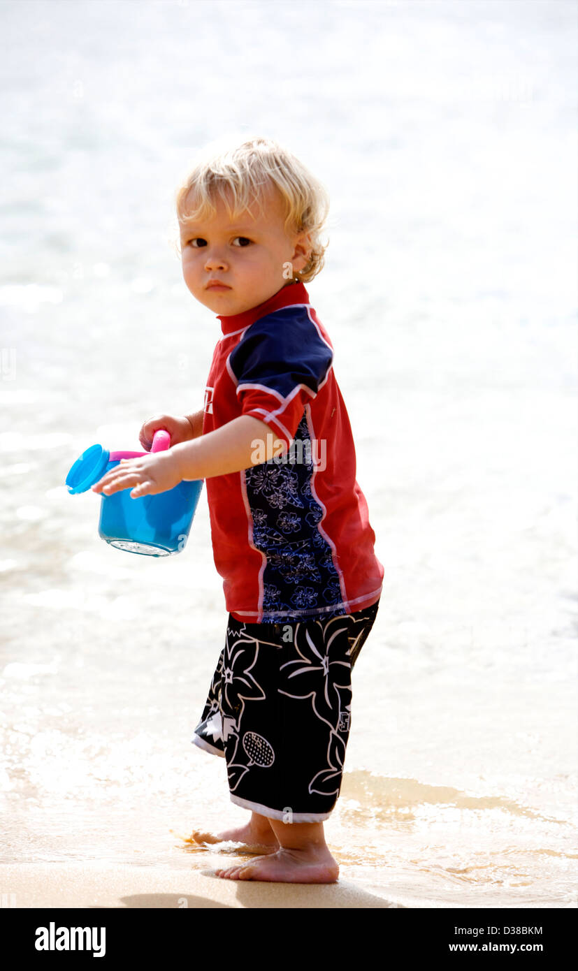 Un piccolo ragazzo giocando sulla spiaggia indossando un rosso e navy sun tuta per proteggerlo dai raggi suns Foto Stock
