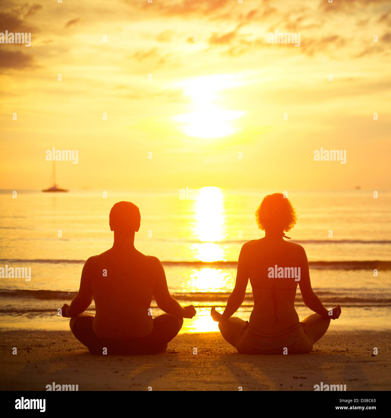 Coppia giovane in una posizione del loto meditando sulla spiaggia al tramonto Foto Stock