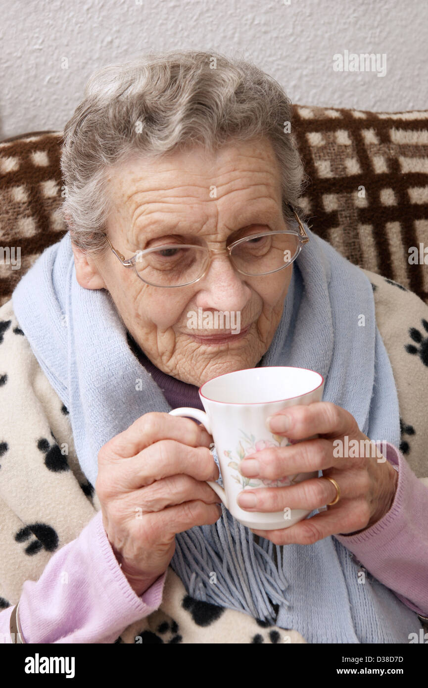 Donna anziana mantenendo calda in inverno avvolto con coperte e una sciarpa avente una bevanda di riscaldamento Foto Stock
