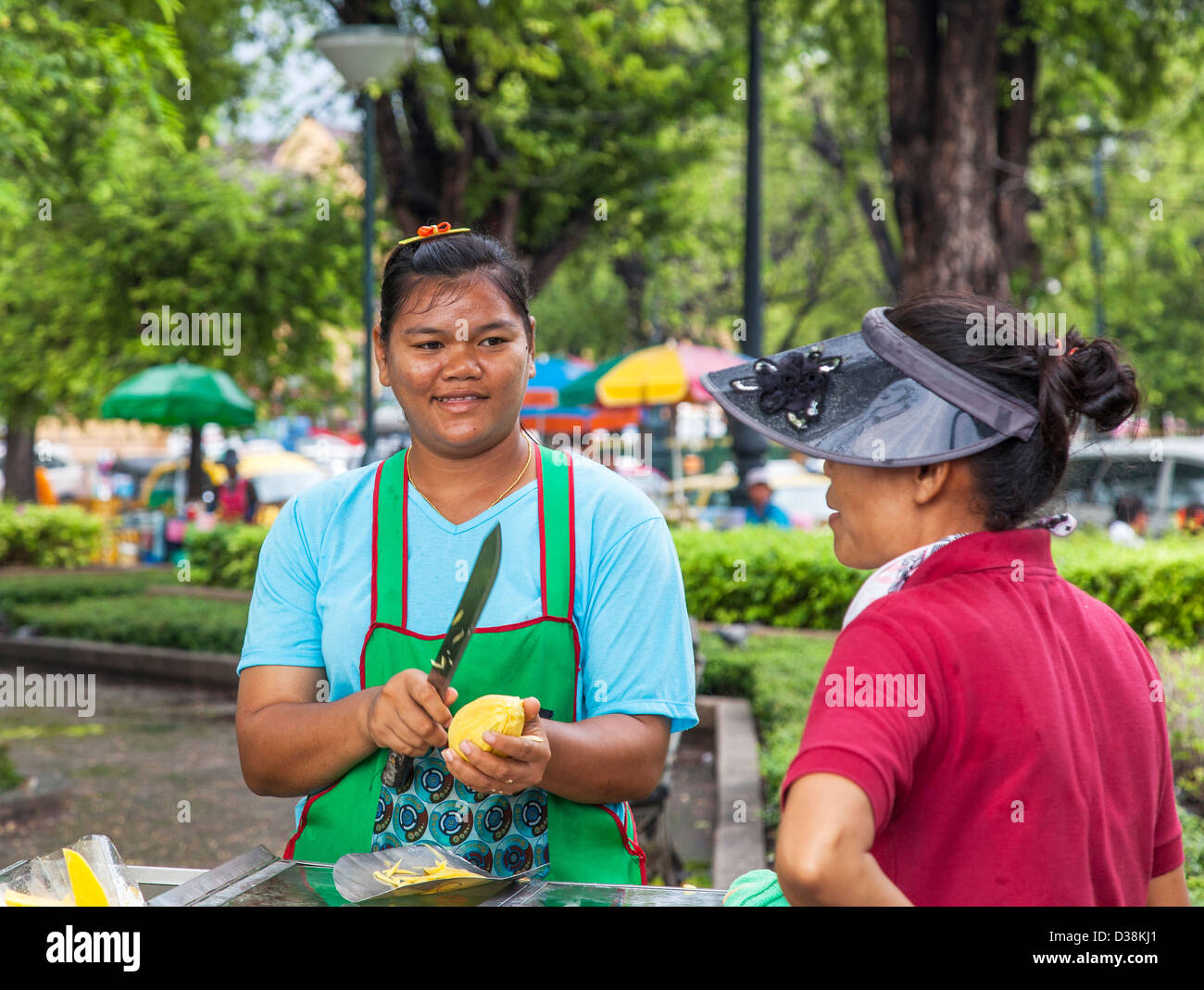 Donna Thai street venditore, peeling e la vendita di frutta, a Bangkok, in Thailandia, per chattare con i suoi amici Foto Stock