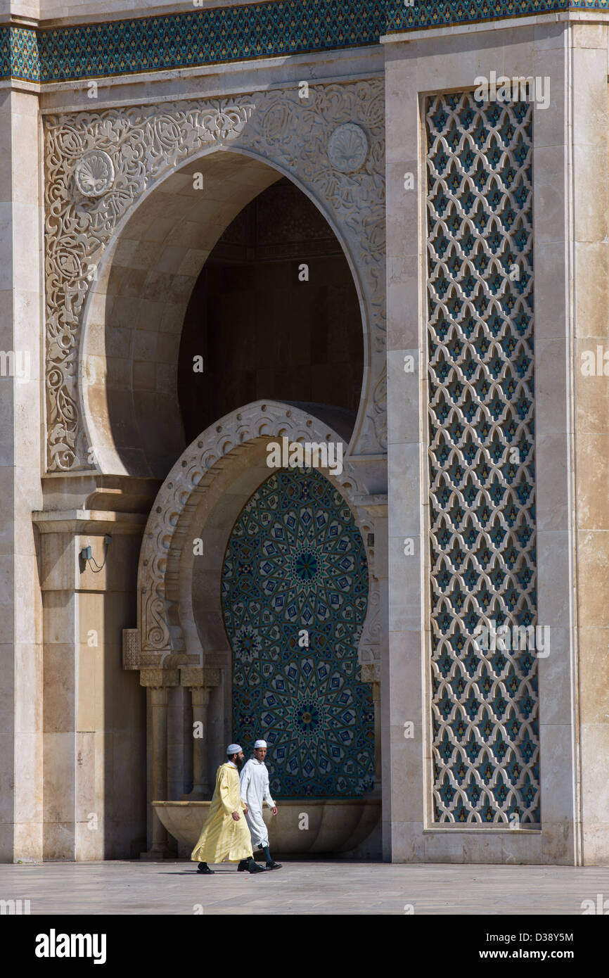 Gli uomini marocchini indossando jalabiyas passato a piedi una delle porte della moschea di Hassan II, Casablanca, Marocco Foto Stock