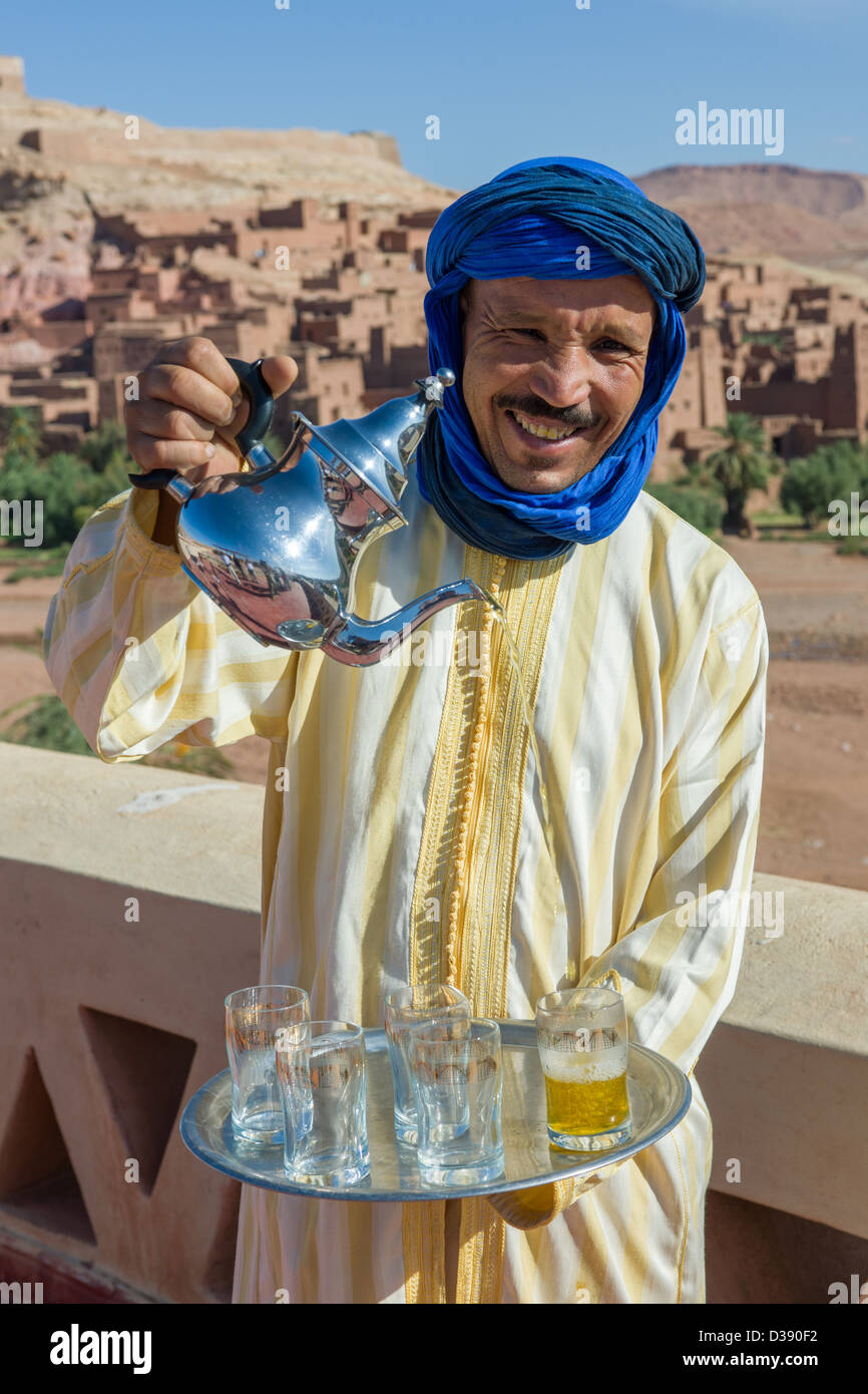 Hussein Boulkil, soprannominato " azione " versando il tè alla menta con il Ksar (borgo fortificato) dietro, Ait Benhaddou, Marocco Foto Stock