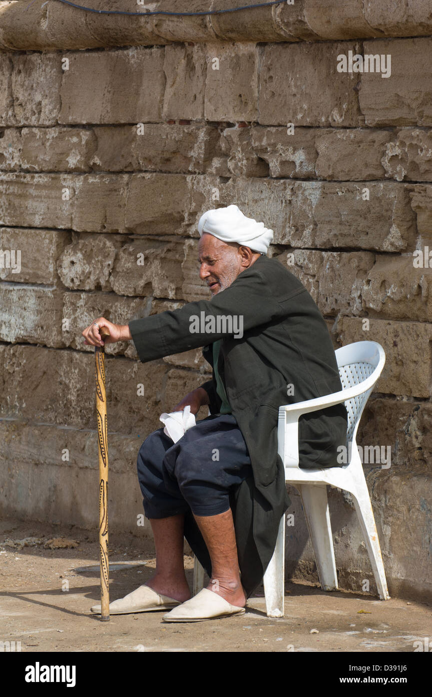 Il vecchio uomo Marocchino con un bastone da passeggio seduto di fronte le mura che circondano il porto di Essaouira, Essaouira, Marocco Foto Stock