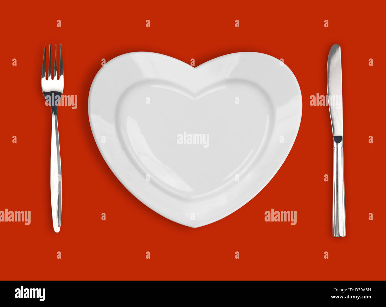 Piastra in forma di cuore, tavola coltello e forchetta su sfondo rosso Foto Stock